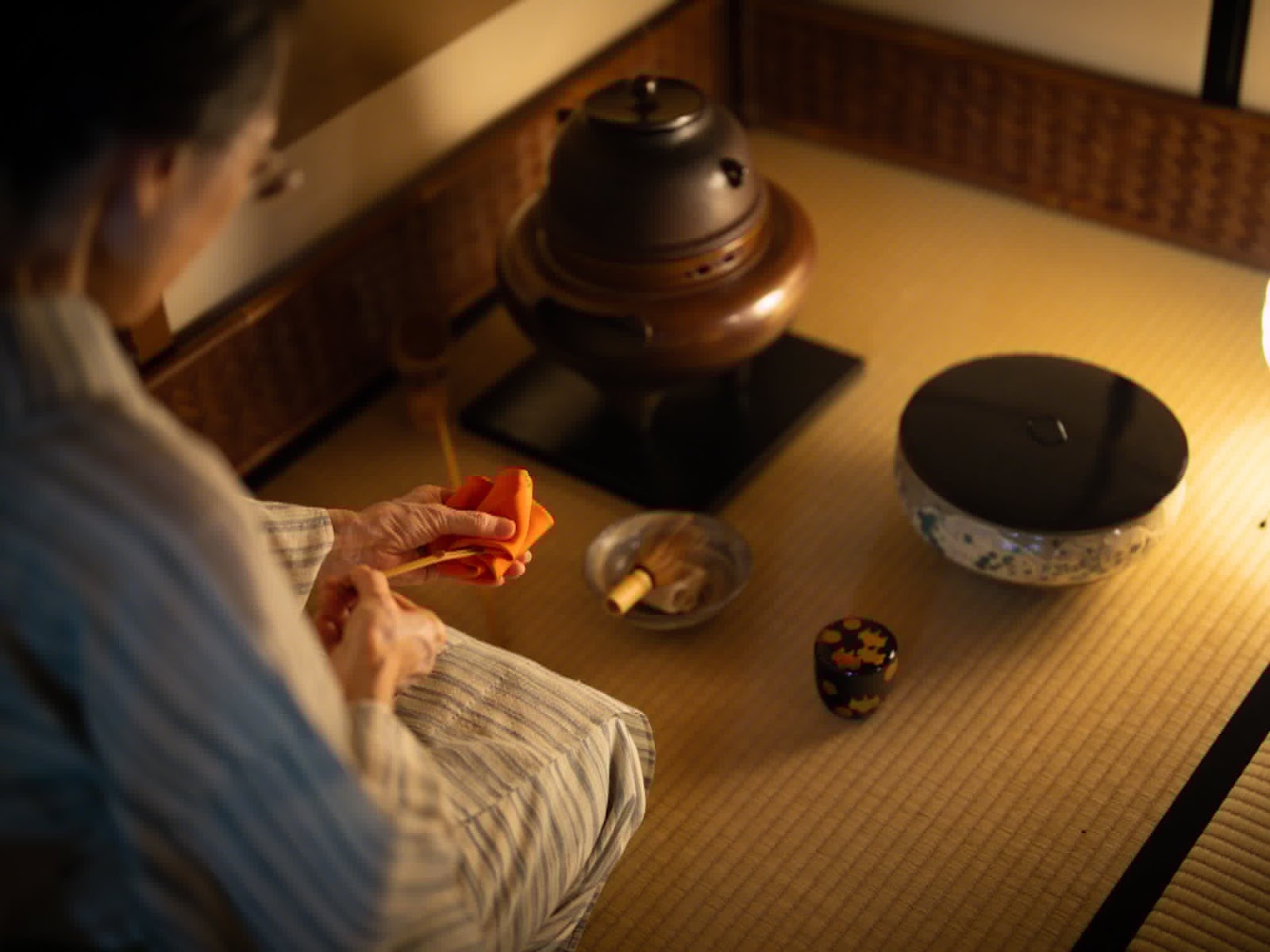 茶室で、袱紗を手に茶釜の前に座る人物